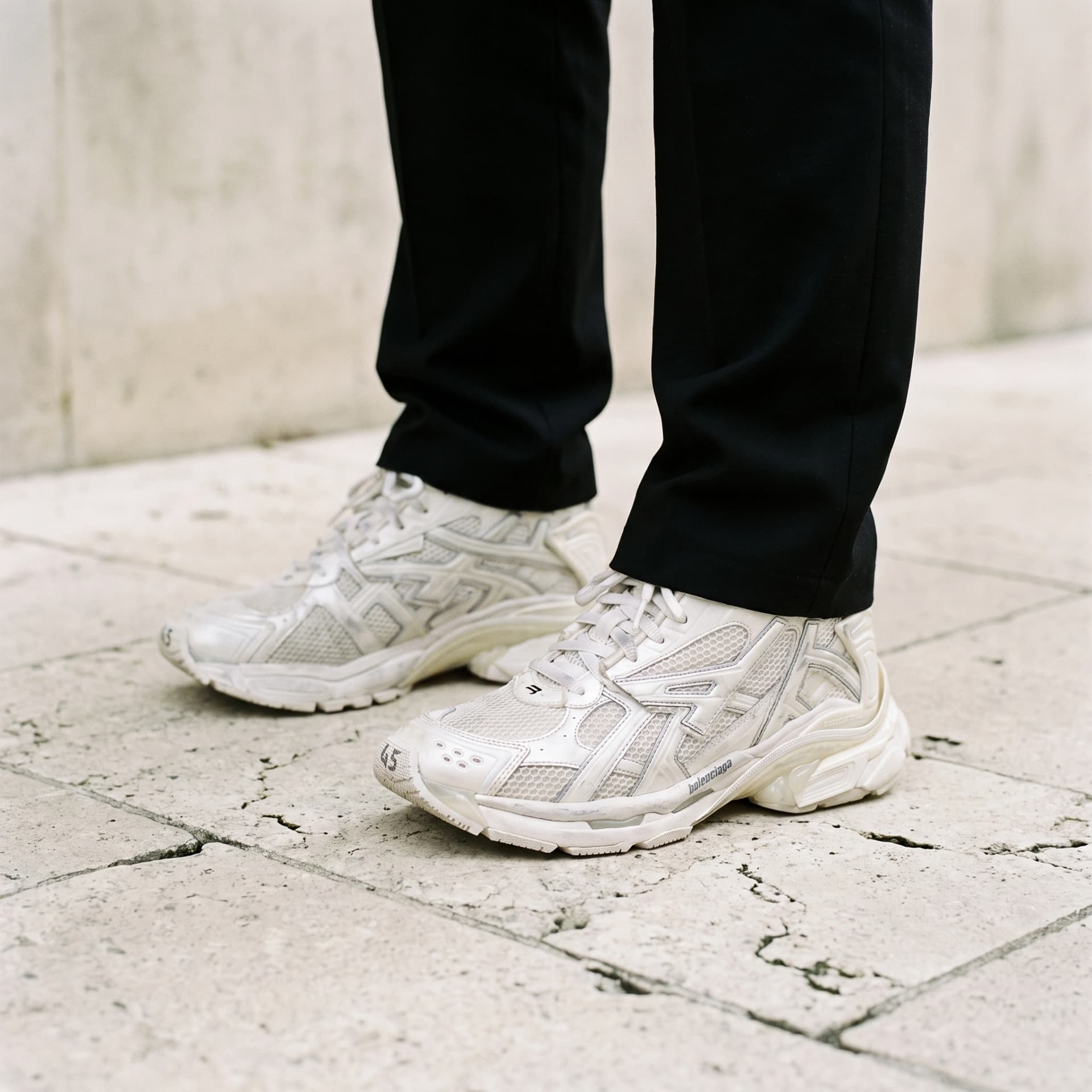 Balenciaga Runner blanche, portées avec un pantalon noir, cadrées des mollets au sol.