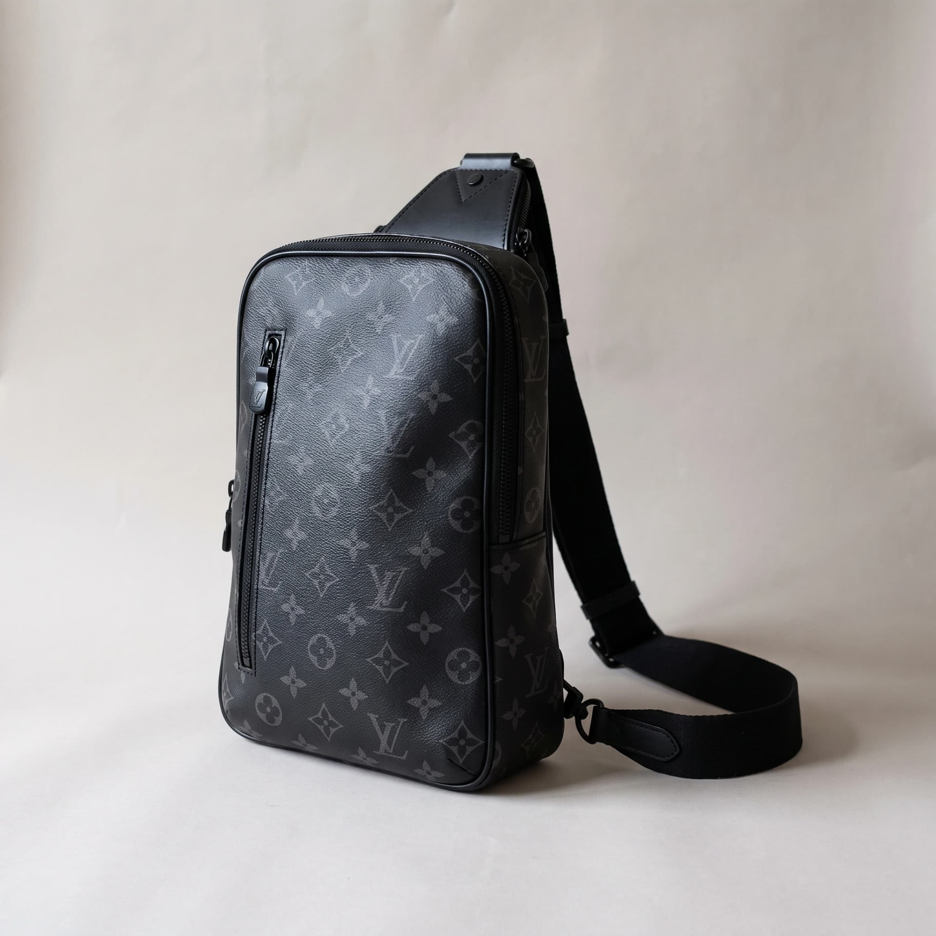 Sac Louis Vuitton Avenue Sling en toile Monogram Eclipse, debout de trois quarts, bandoulière posée à côté.