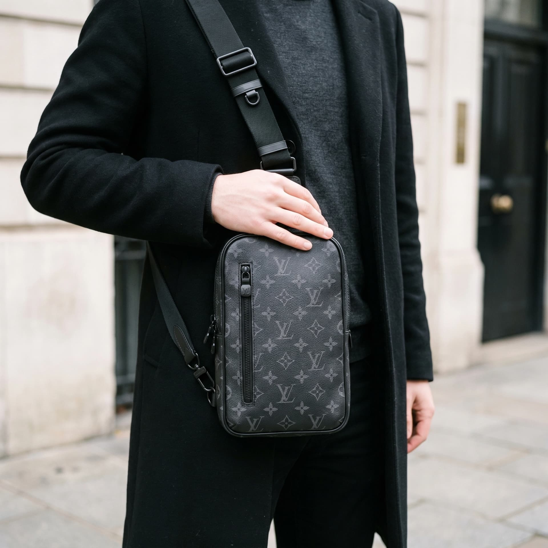 L'Avenue Sling porté en travers de la poitrine sur un manteau noir, cadré sans visage.