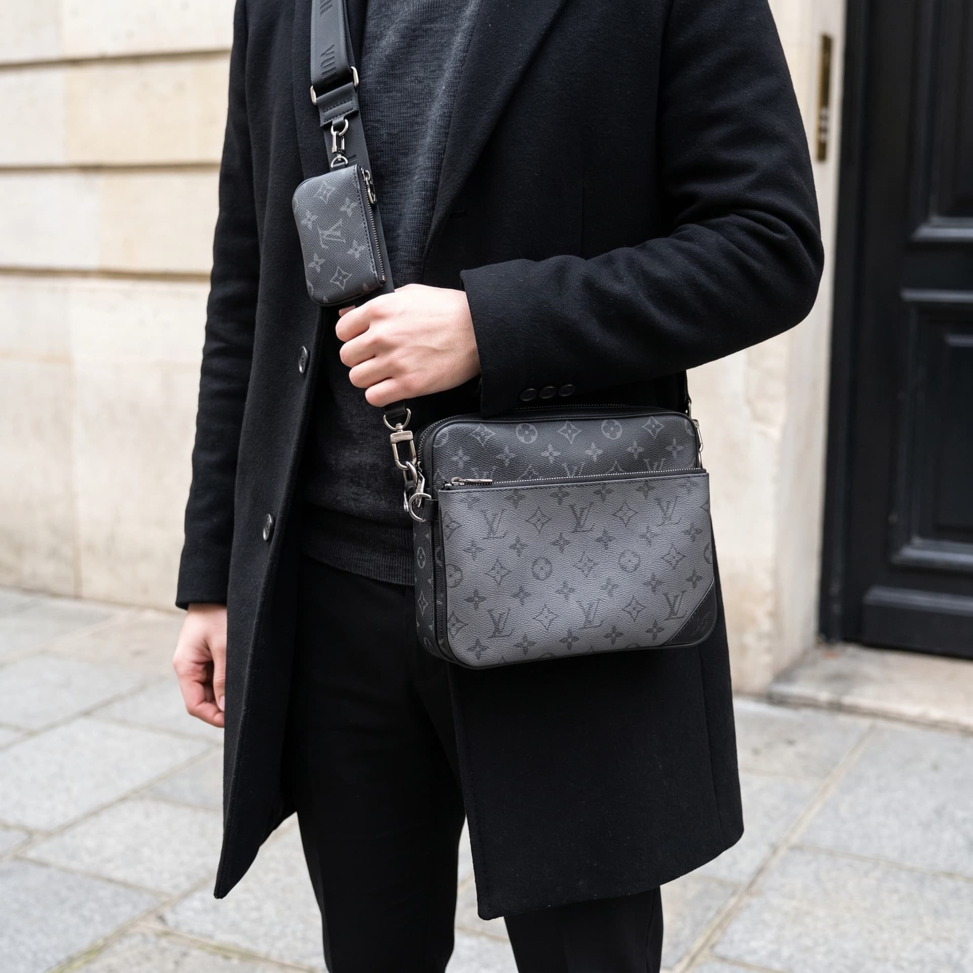 Le Trio Messenger porté en bandoulière sur un manteau noir, cadré sans visage.